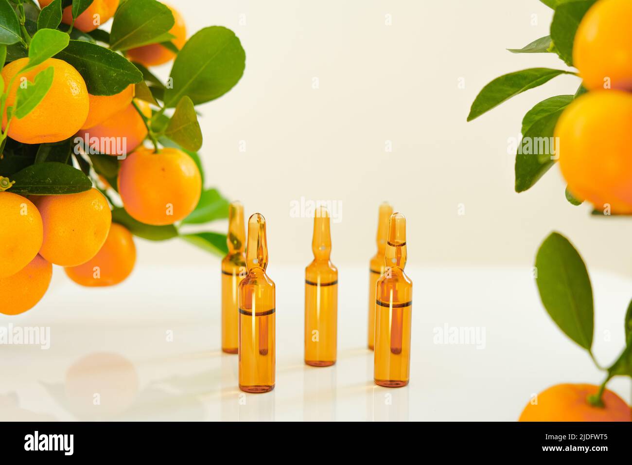 Vitamina C. ampolle di vetro con una soluzione di vitamina C e cespugli di mandarino su sfondo chiaro.bellezza e salute. Agrumi con foglie verdi. Foto Stock