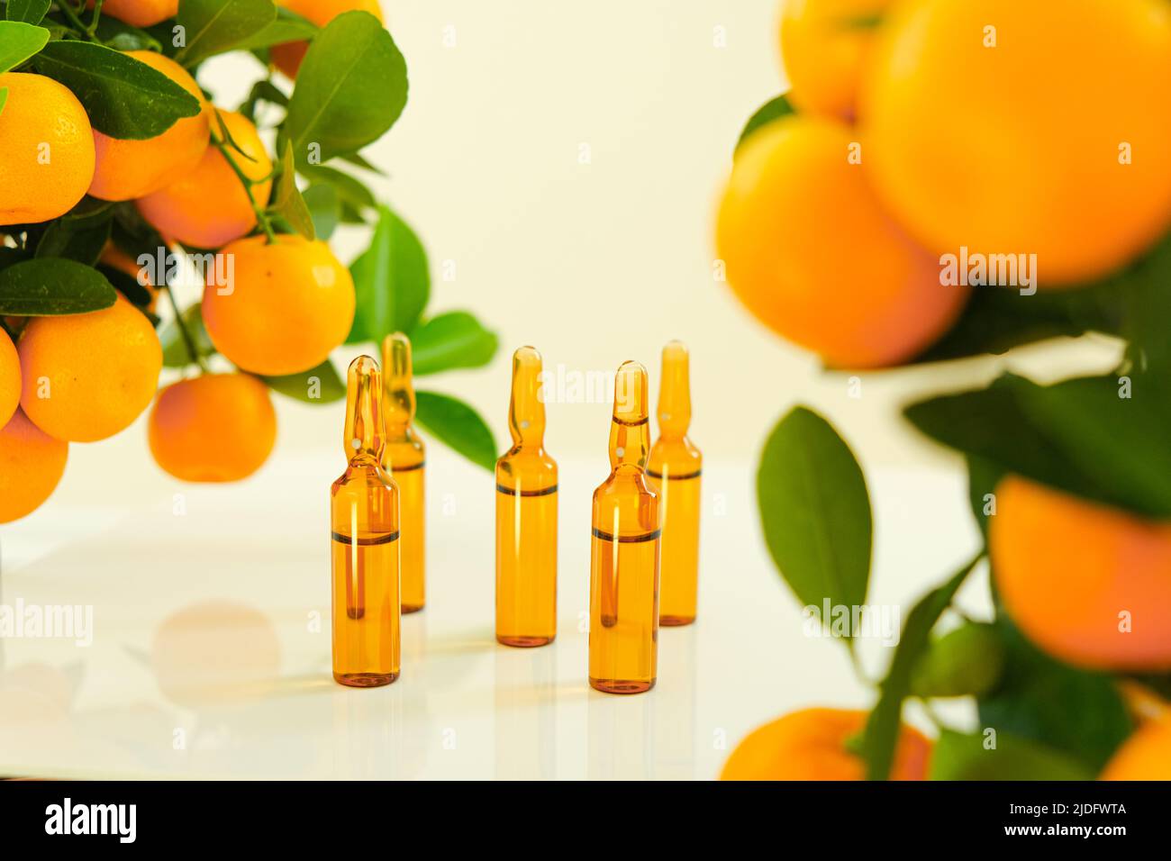 Vitamina C .fiale di vetro marrone con una soluzione di vitamina C e cespugli di mandarino su sfondo chiaro.bellezza e salute. Agrumi con verde Foto Stock