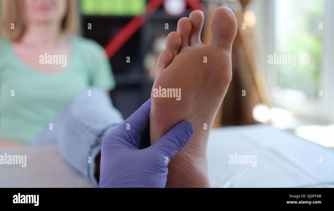 Medico podiatrist in guanti sterili che esaminano il piede femminile Foto Stock