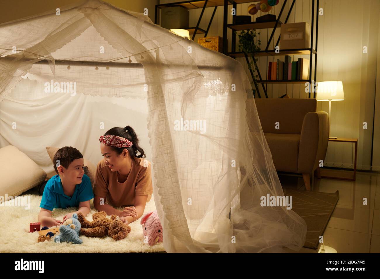 Madre allegra e figlio che giocano all'interno di una grande tenda che hanno installato in camera da letto Foto Stock