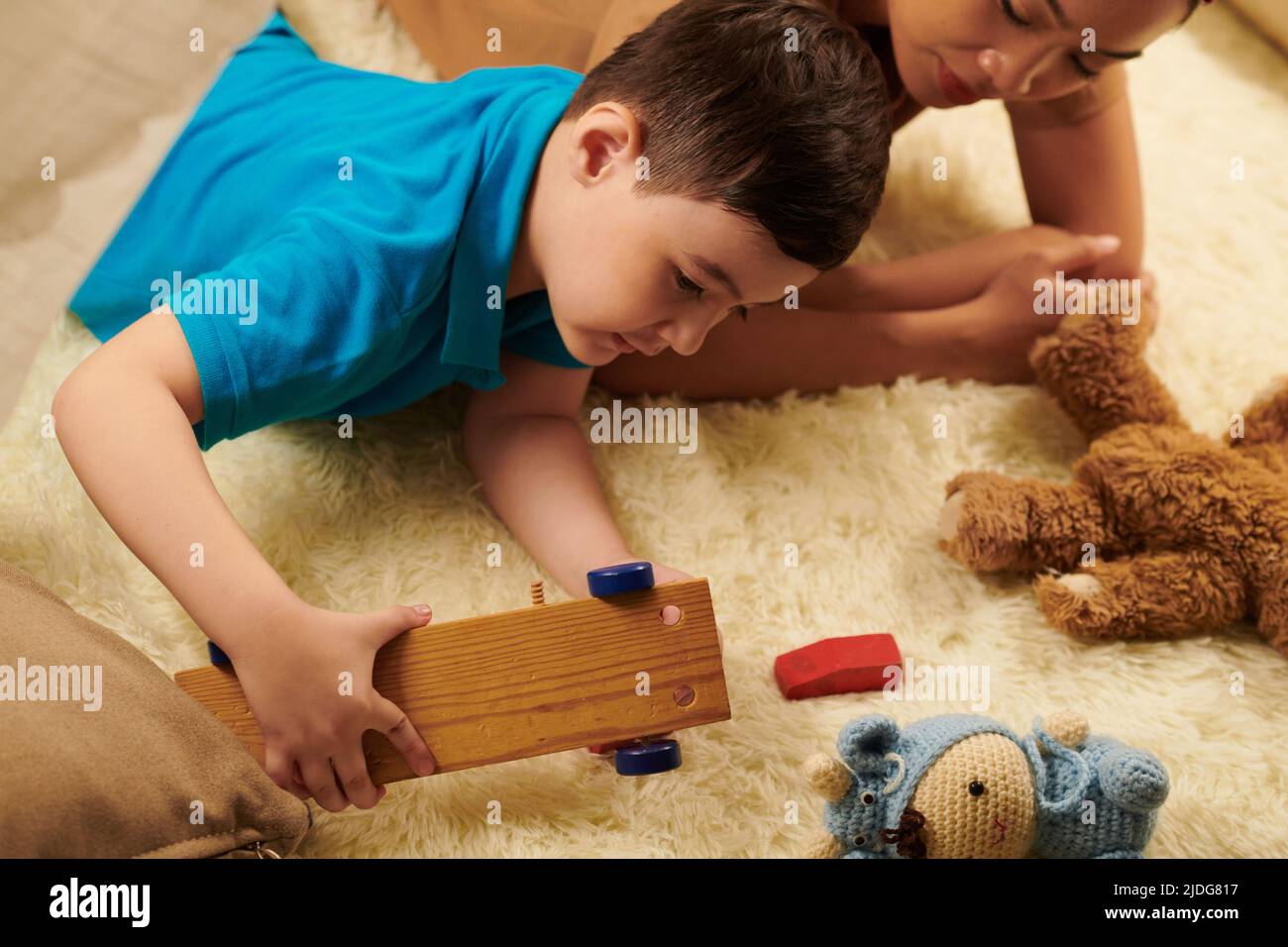 Ragazzo che gioca con vari giocattoli su tappeto di pelliccia a casa Foto Stock