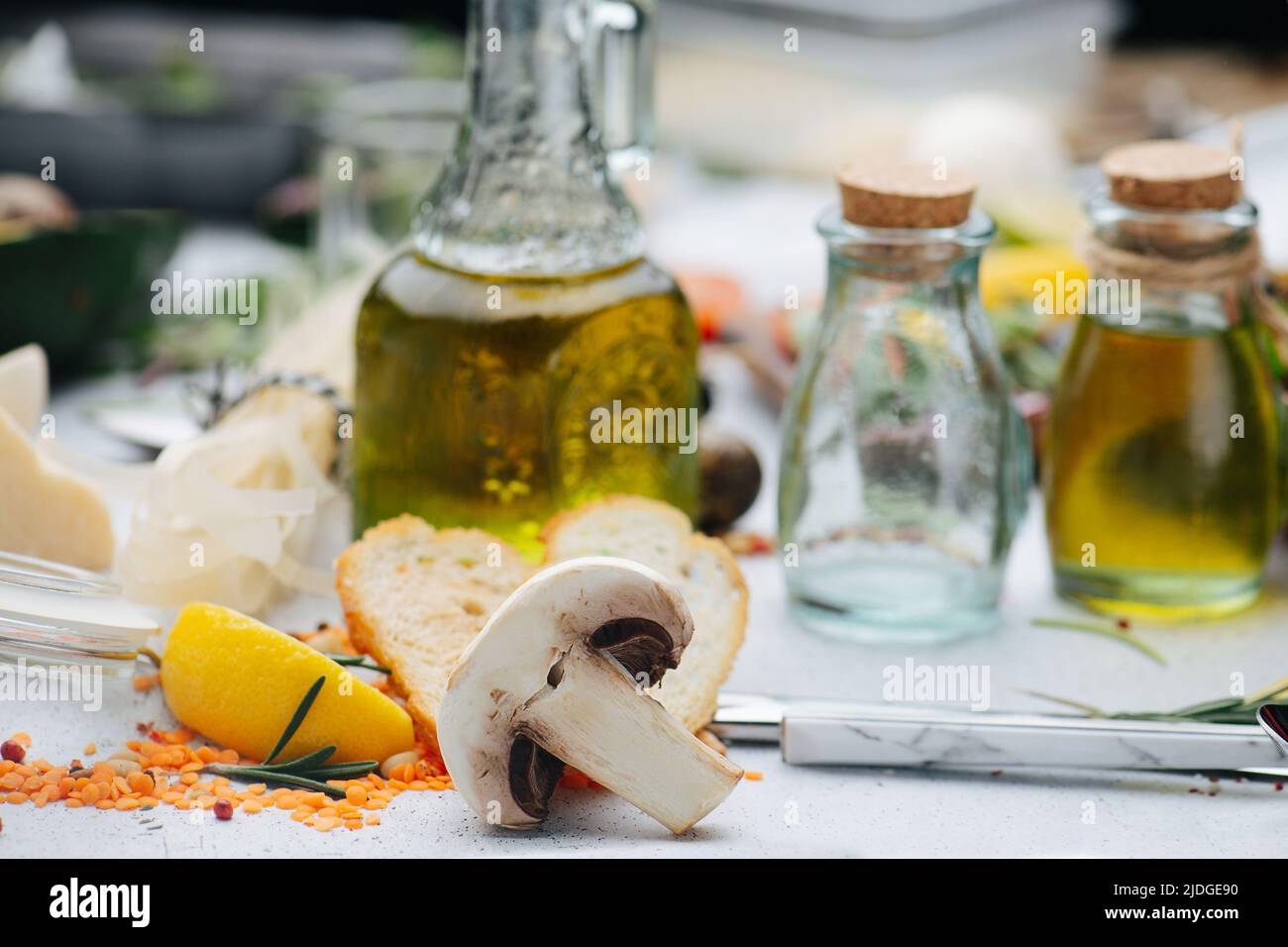 Mezza di funghi Champingnon davanti alle bottiglie d'olio e ad altri ingredienti da cucina sul tavolo. Sfondo parzialmente sfocato. Foto Stock