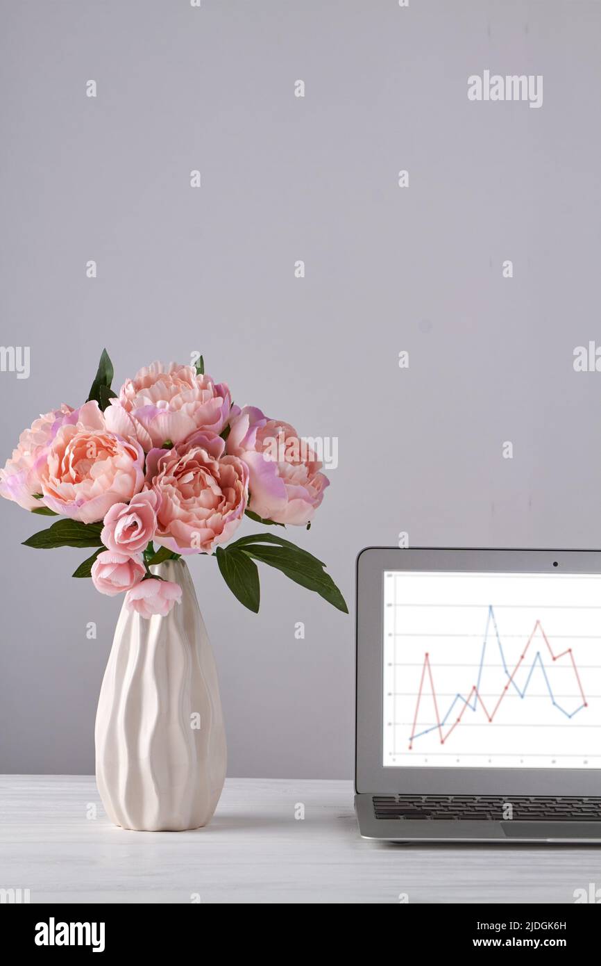 Vaso di peonie rosa e laptop con carte. Sfondo bianco verticale. Foto Stock