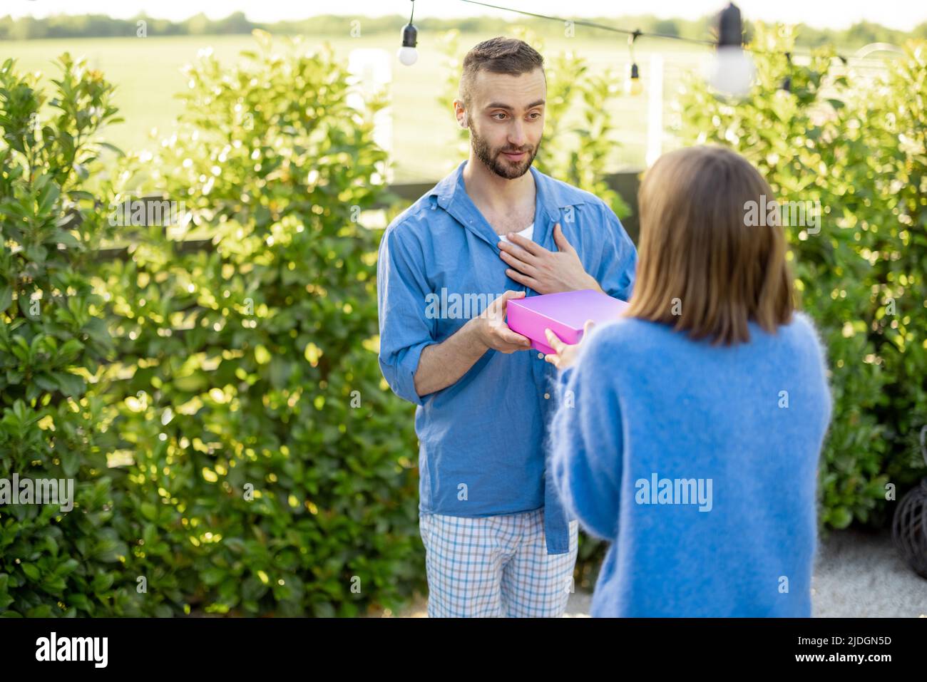 L'uomo dà un regalo in scatola rosa alla sua donna, celebrando all'aperto Foto Stock