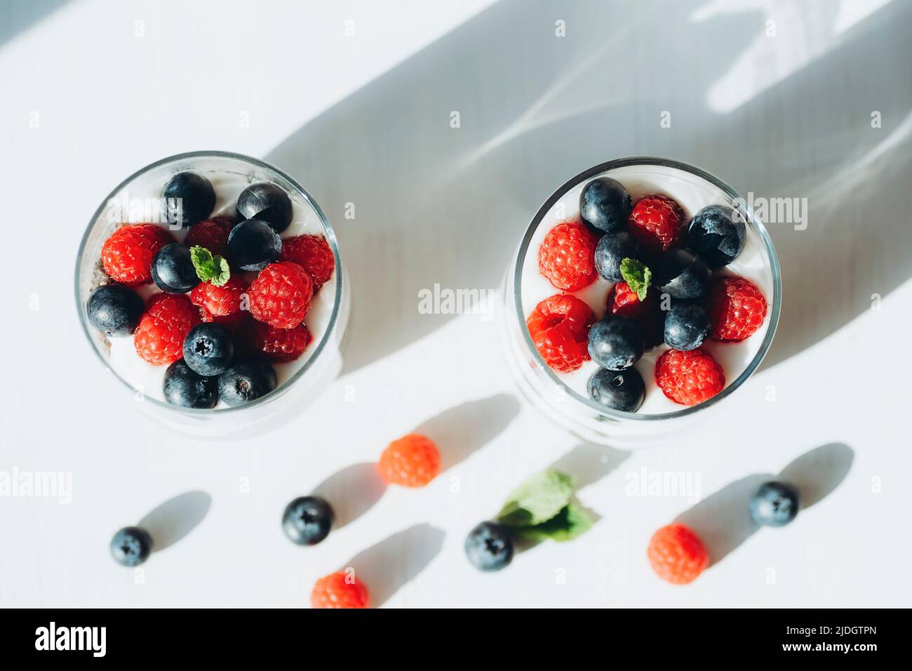 Due bicchieri di budino chia con lampone fresco e mirtillo su tavola bianca, vista dall'alto. Foto Stock