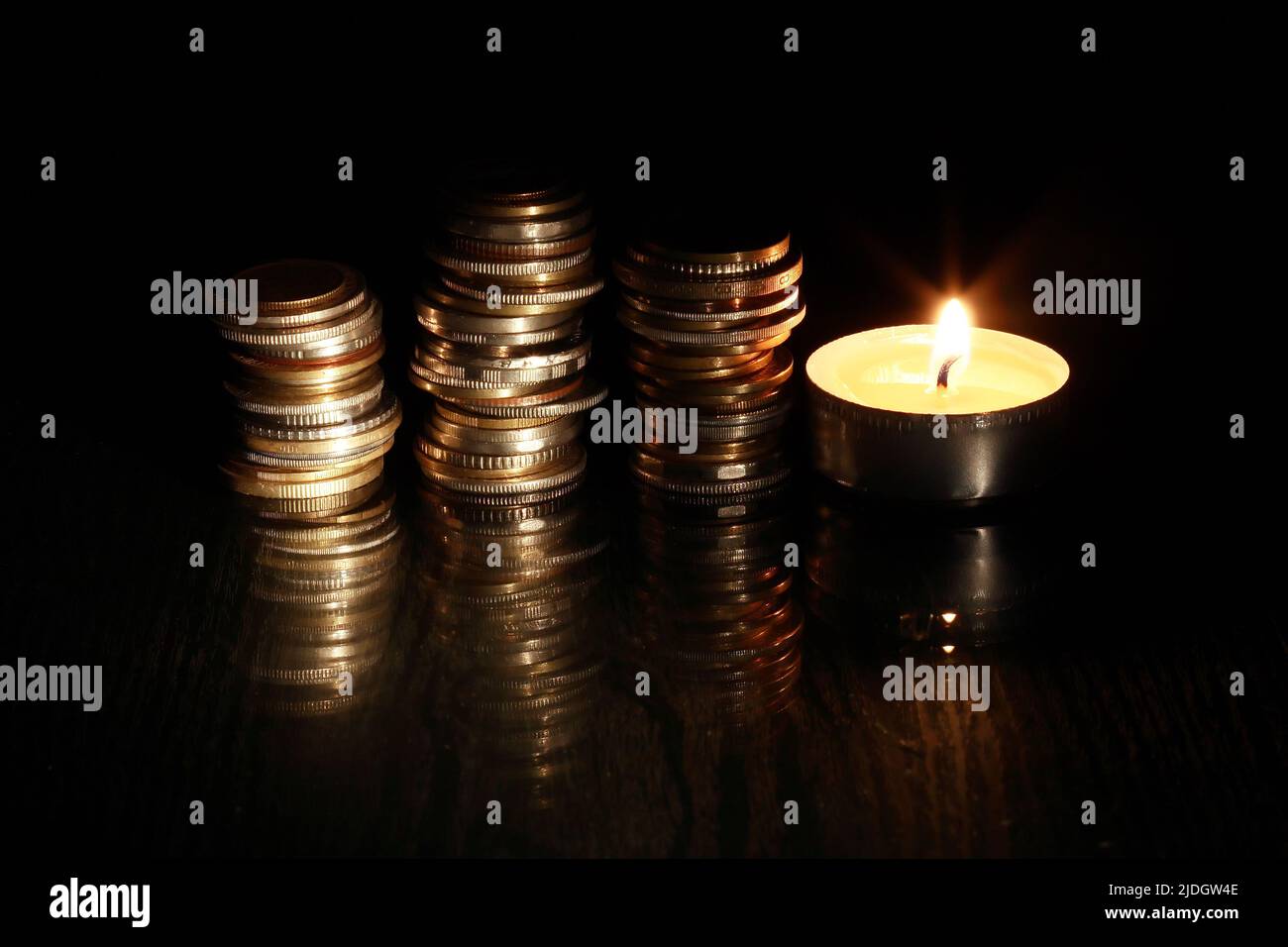 Set di monete vicino illuminazione candela su sfondo scuro Foto Stock