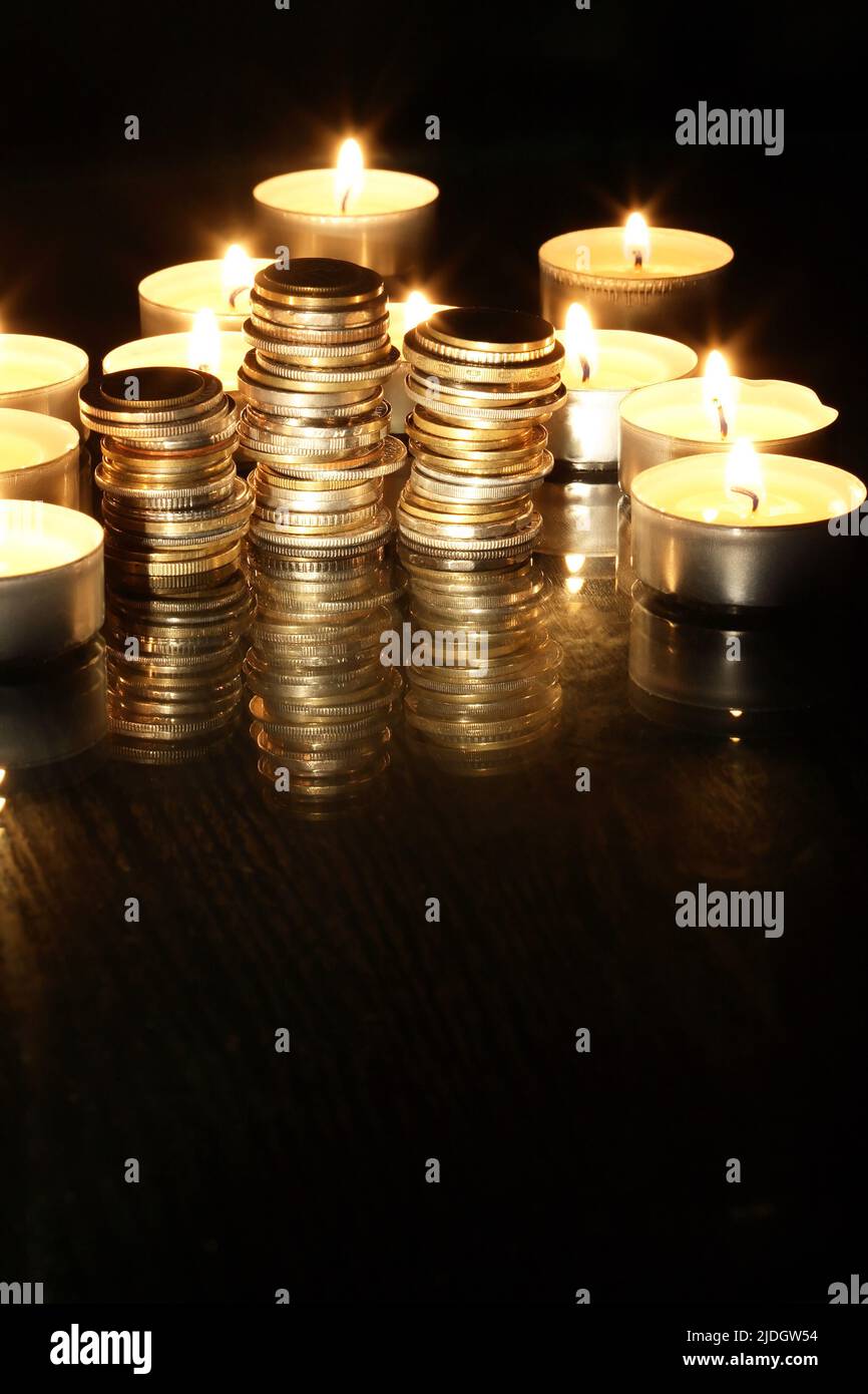 Set di monete tra le candele di illuminazione su sfondo scuro Foto Stock