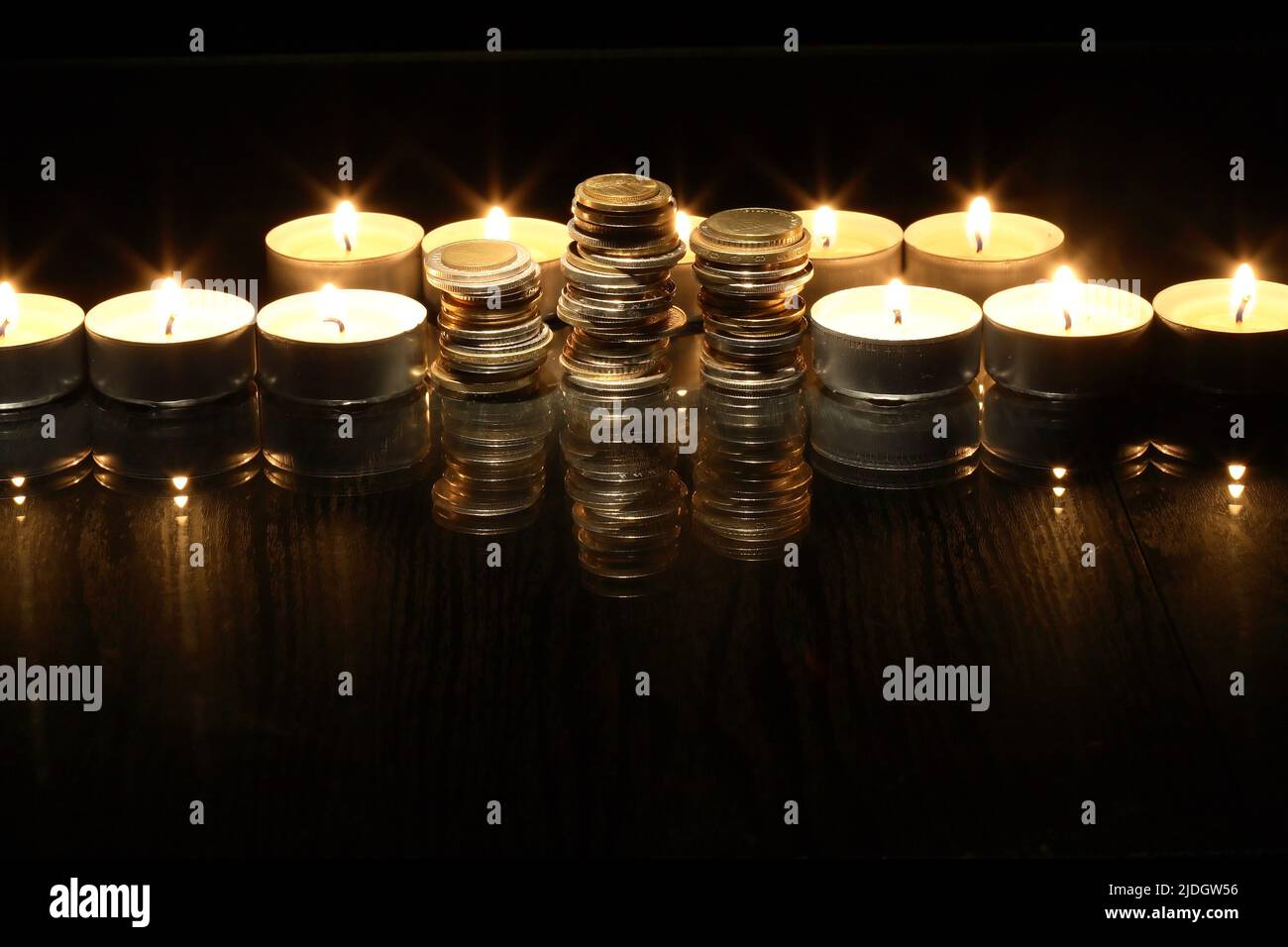 Set di monete tra le candele di illuminazione su sfondo scuro Foto Stock
