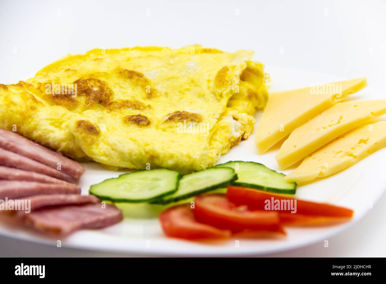 Gustosa colazione o pranzo con omelette con salsiccia, pomodoro, cetriolo e pezzi di formaggio sul piatto bianco. Foto Stock