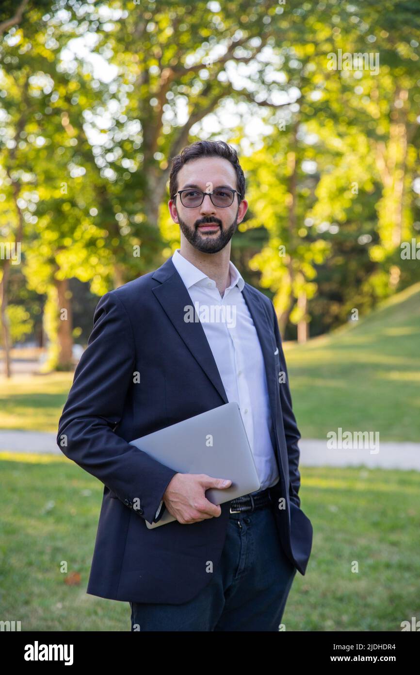 ritratto di un elegante uomo d'affari caucasico che posava tenendo il suo laptop e guardando via Foto Stock