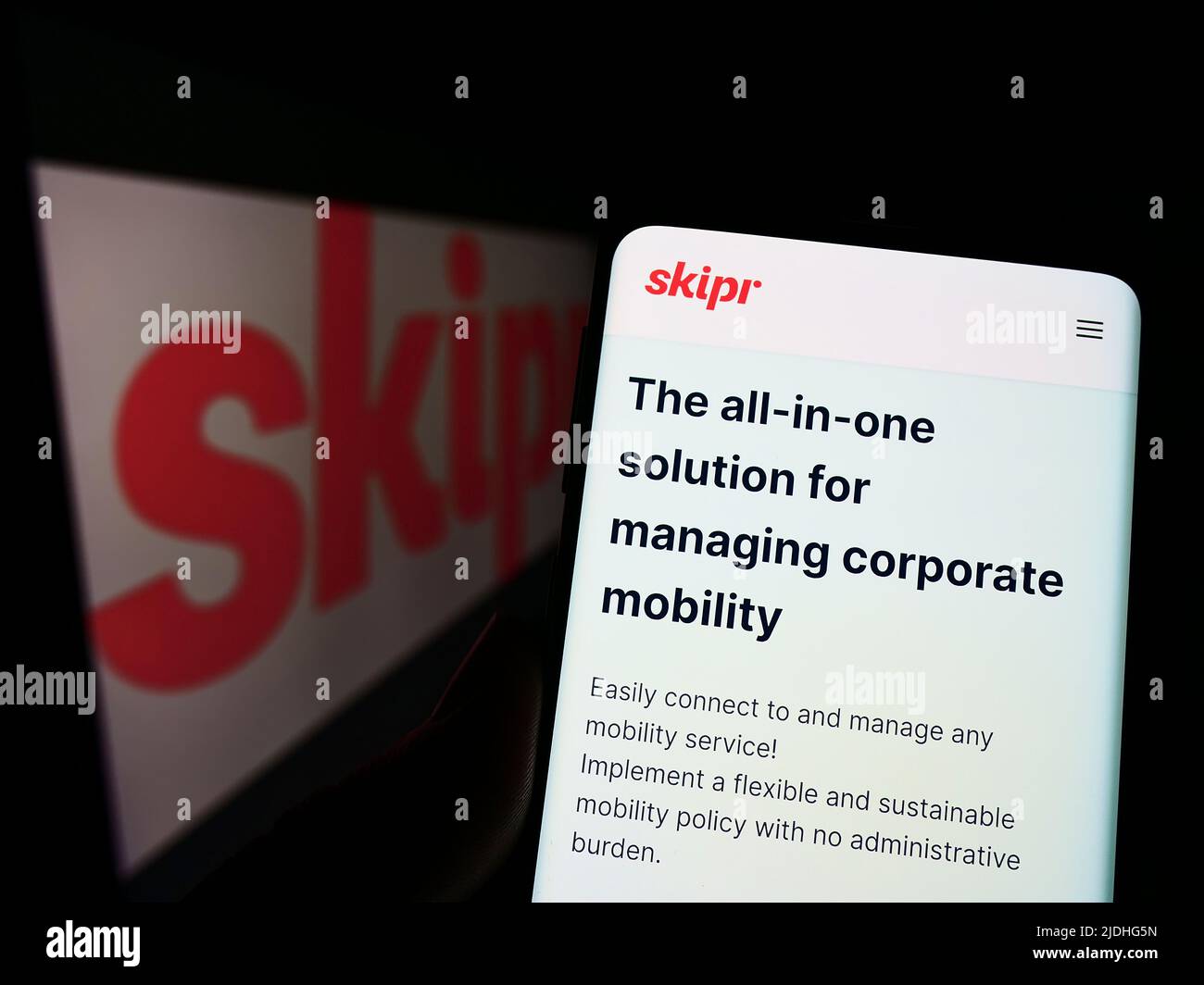 Persona che detiene il cellulare con il sito web della società belga di mobilità Skipr SA sullo schermo di fronte al logo. Concentrarsi sul centro del display del telefono. Foto Stock