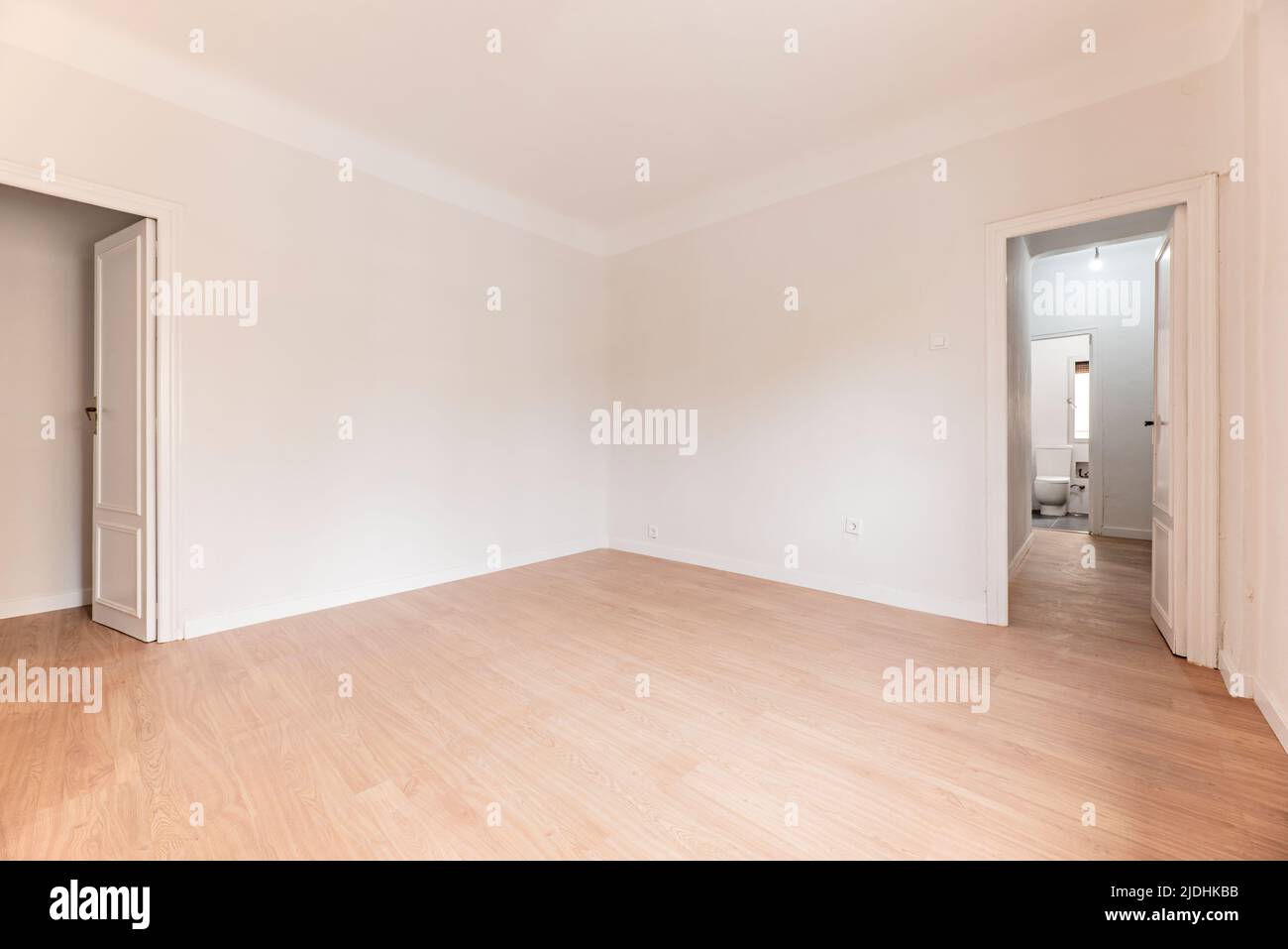 Camera vuota con pavimento in parquet di quercia, pareti dipinte di bianco e legno bianco e bagno in un'altra stanza Foto Stock