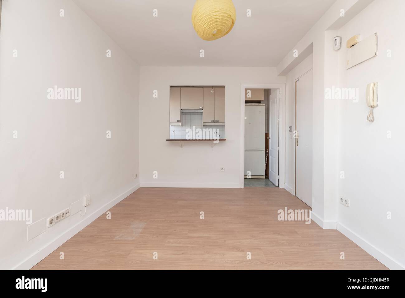 Soggiorno vuoto con pavimento in parquet di quercia, pareti dipinte di bianco e portello di servizio dalla cucina Foto Stock
