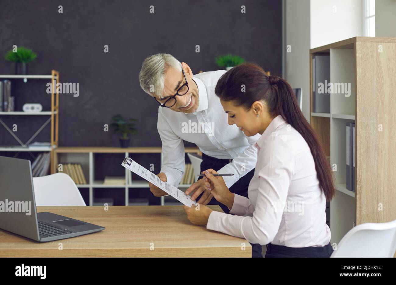 Sorridente dipendente senior che dà il documento al giovane manager per la firma Foto Stock
