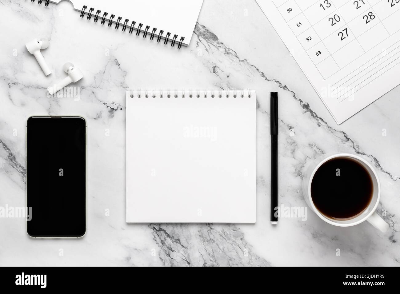 Tazza di caffè, telefono, cuffie, calendario e carta per notebook sul tavolo in marmo. Sfondo bianco e nero con spazio di copia, mockup. Design piatto, pl Foto Stock
