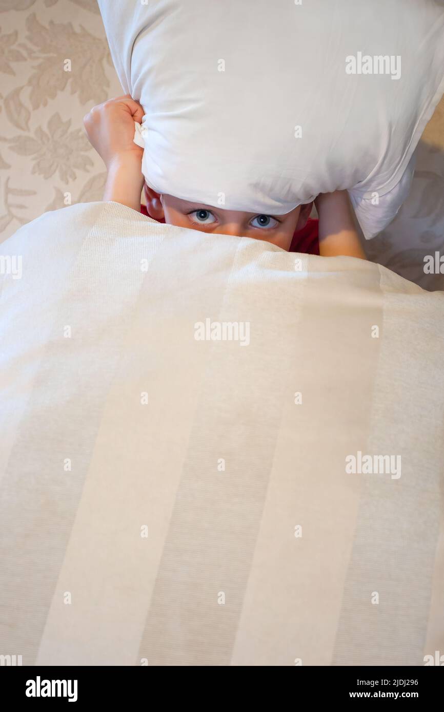Ragazzo che si nasconde dietro i cuscini solo gli occhi visibili Foto Stock