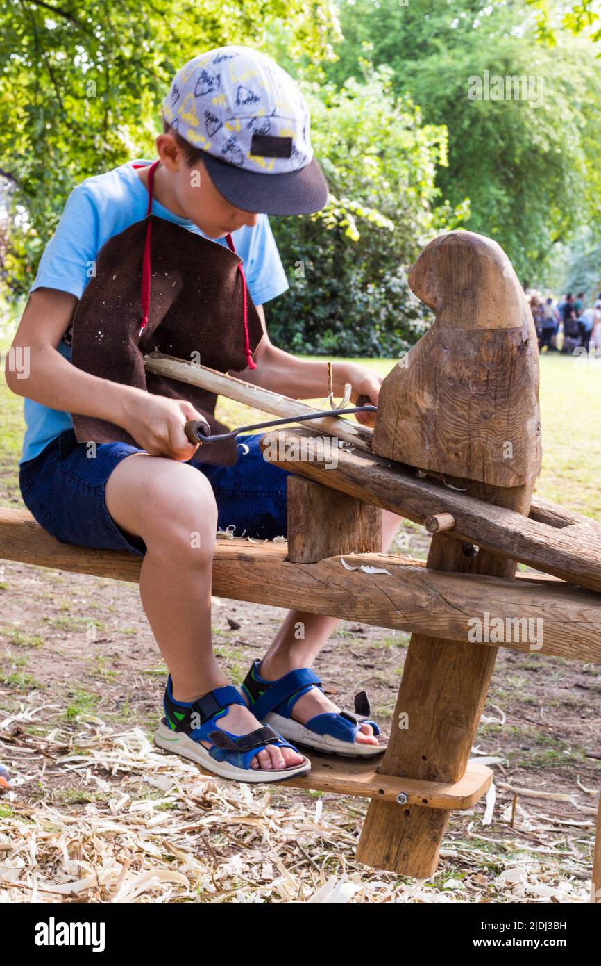 Bambino ragazzo che rasa ramo di legno con attrezzi tradizionali al Tunderfesztival 2022, Sopron, Ungheria Foto Stock