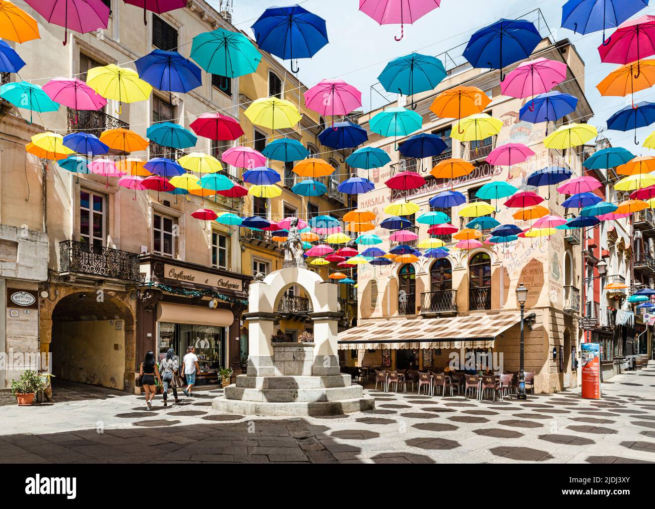 Gli ombrelloni colorati proteggono i passanti in Piazza Lamarmora, circondata da case storiche nel centro storico di Iglesias, nel sud-ovest della Sardegna, Italia Foto Stock