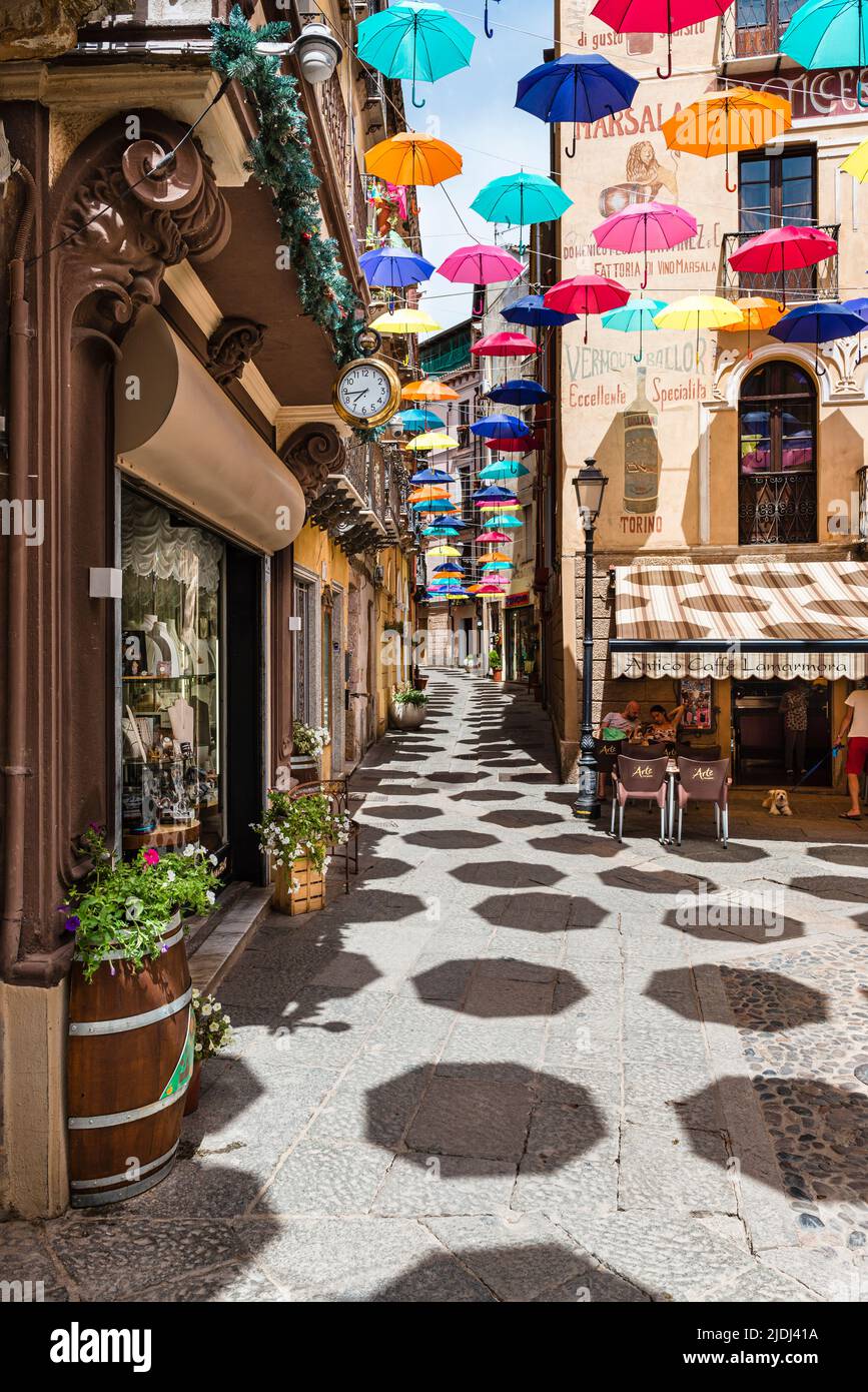 Gli ombrelloni colorati proteggono i passanti in Piazza Lamarmora, circondata da case storiche nel centro storico di Iglesias, nel sud-ovest della Sardegna, Italia Foto Stock