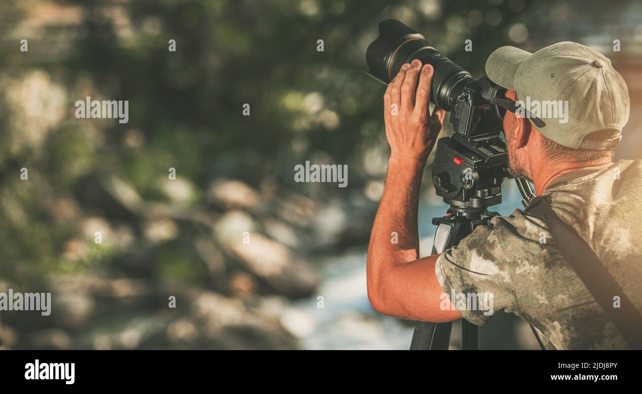 Fotografo maschio caucasico che prende un colpo nel mezzo della natura selvaggia usando la sua macchina fotografica e treppiede. Stagione estiva. Sfondo sfocato. Foto Stock