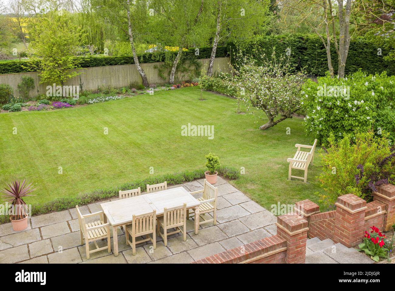 Patio giardino con mobili su una terrazza in un giardino inglese con giardino sul retro con grande prato Foto Stock