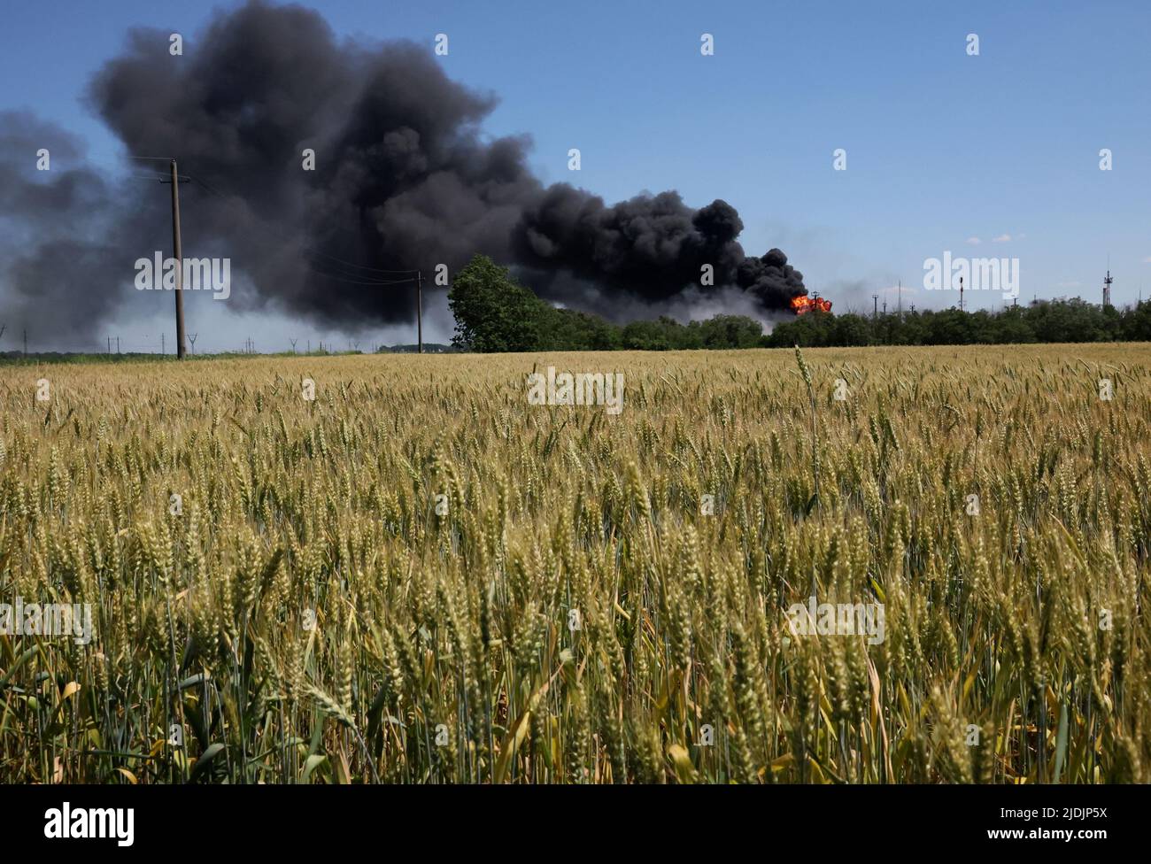 Un incendio proveniente da un impianto di lavorazione del gas continua a bruciare dietro un campo di grano dopo che l'impianto è stato colpito dalla sgranatura pochi giorni prima ad Andriivka, nella regione di Kharkiv, mentre l'attacco della Russia all'Ucraina continua in Ucraina, il 21 giugno 2022. REUTERS/Leah Millis Foto Stock