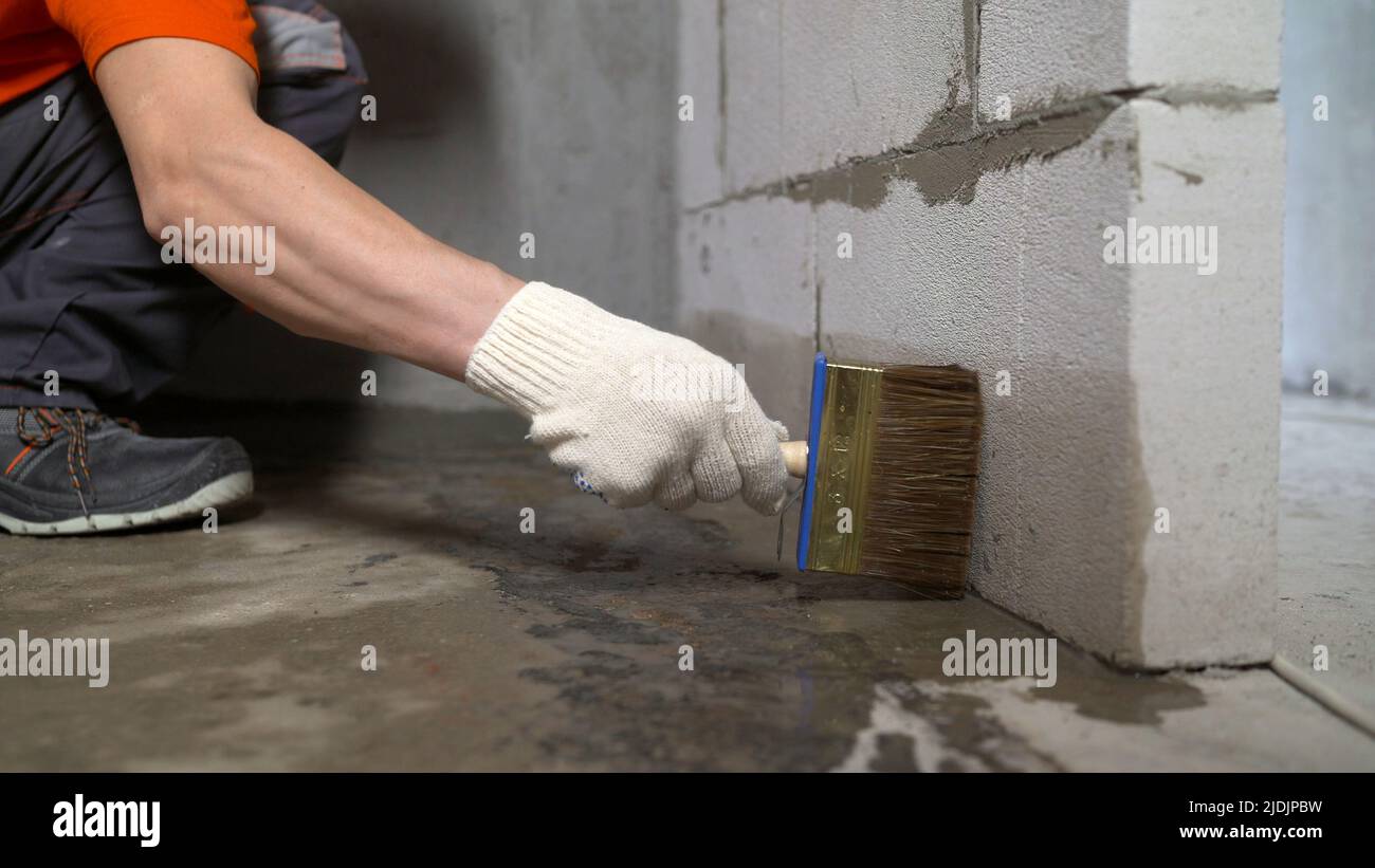 Fondo per pavimenti in calcestruzzo per impermeabilizzazione. Il lavoratore bagna il pavimento di calcestruzzo con un pennello. Foto Stock