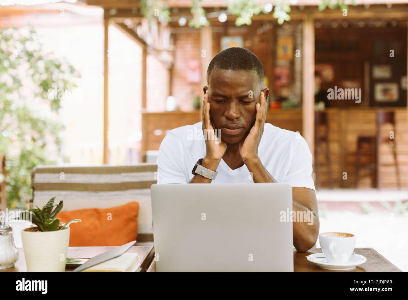 Serio uomo d'affari multirazziale che usa un laptop in un caffè con la testa nelle mani in un caffè. Videochiama e leggi le informazioni finanziarie Foto Stock