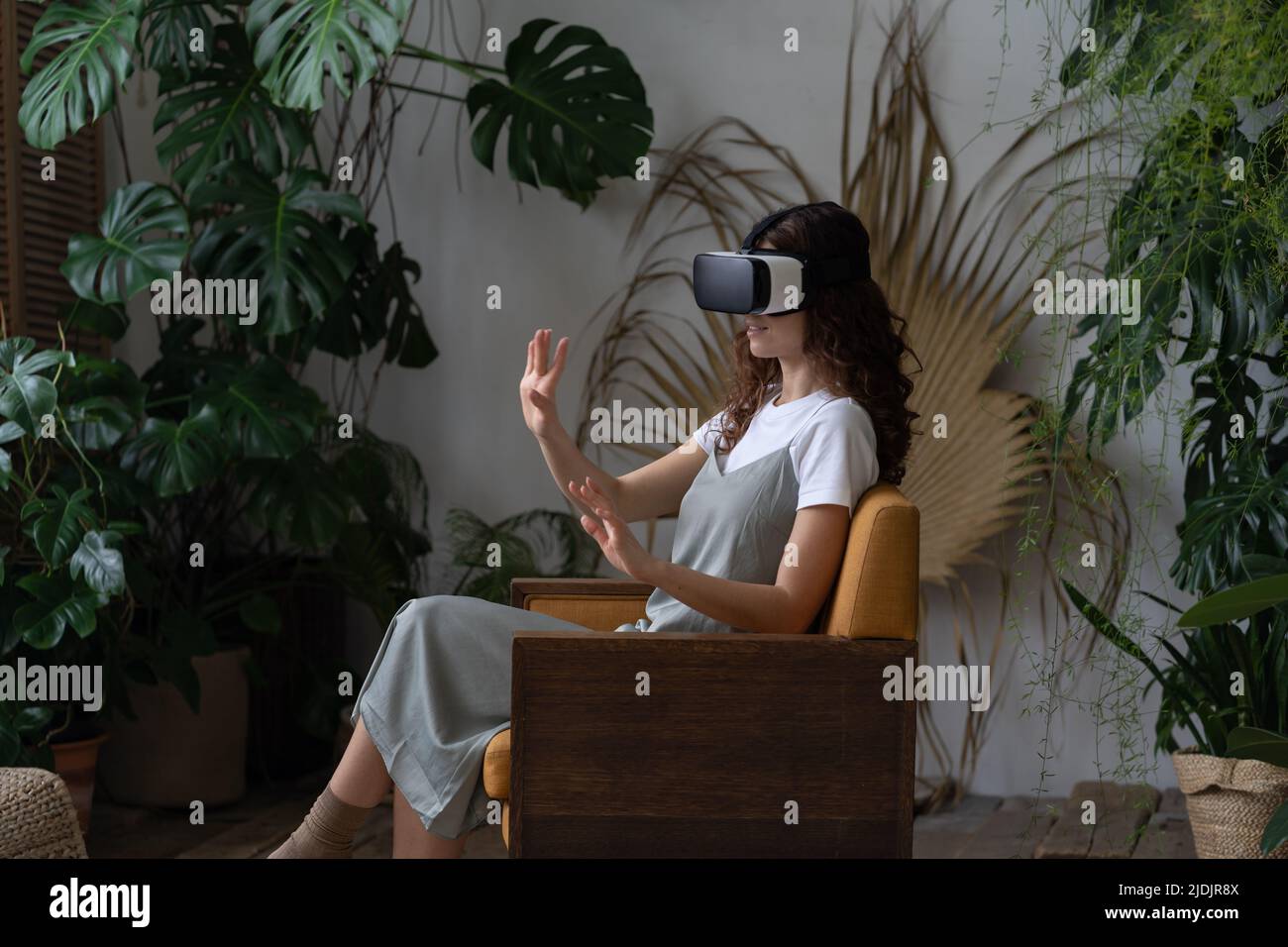 Giovane donna che indossa il casco VR sperimentando la realtà virtuale mentre riposa in serra Foto Stock