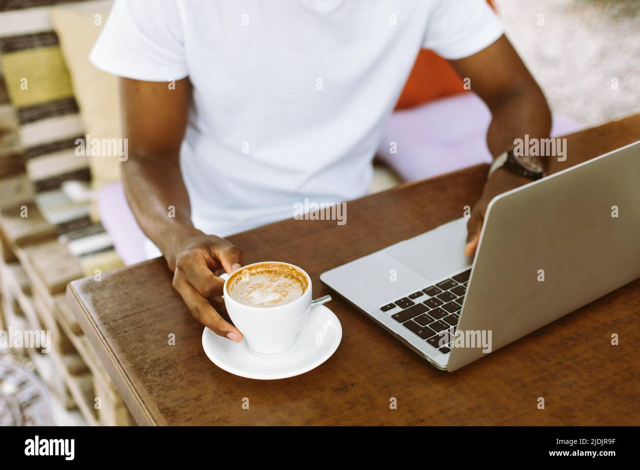 Uomo multiculturale unrecogniable che usa il laptop, prendendo le note nel libro degli esercizi, bere il caffè durante lo studio di tirocinio Foto Stock