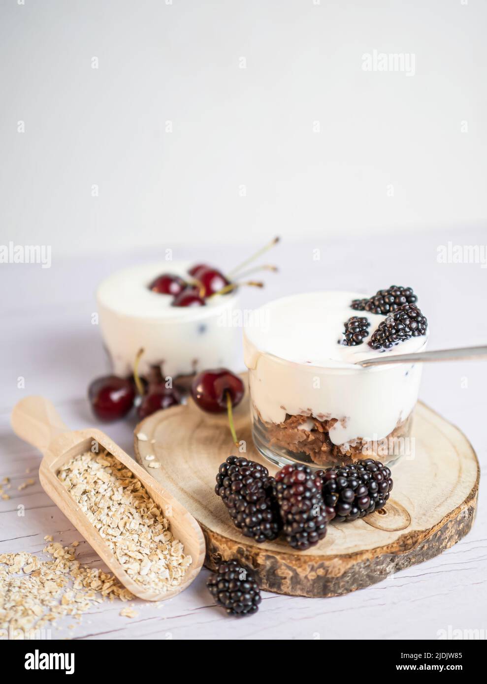 Yogurt con more e ciliegie, frutta fresca con biscotto all'avena, fondo in legno bianco. Foto Stock