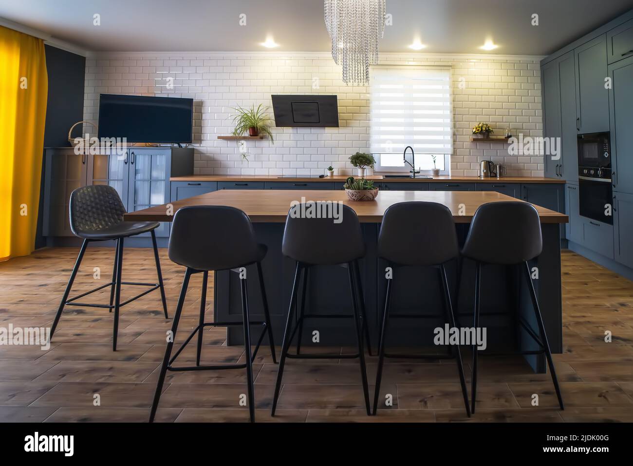 Interno di cucina moderna con pavimento in legno e grande tavolo al centro della stanza. Foto Stock