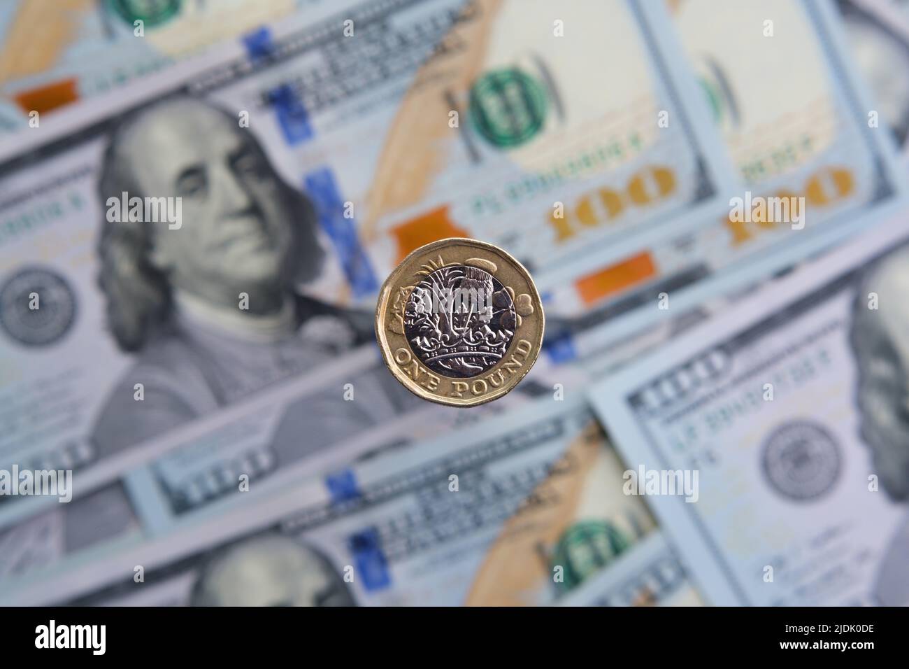 Moneta britannica da un libbra in primo piano e blurred banconote del dollaro di hunder sullo sfondo. Concetto di inflazione. Non un montaggio, foto reale. Foto Stock