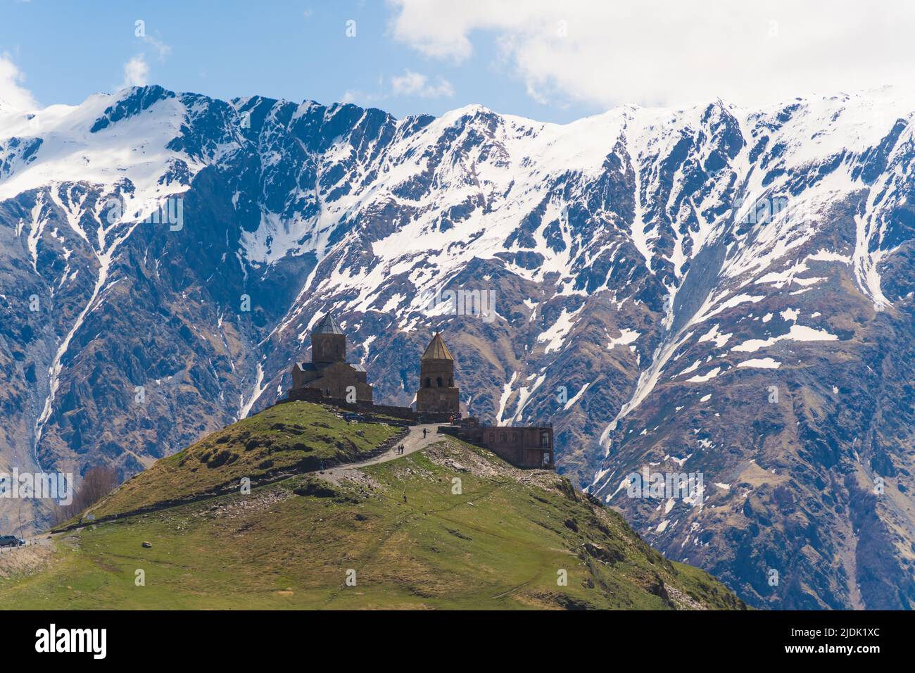 Bella vista dell'antica chiesa della Trinità di Gergeti a Kazbegi, Georgia. Montagne innevate del Caucaso sullo sfondo. Foto di alta qualità Foto Stock