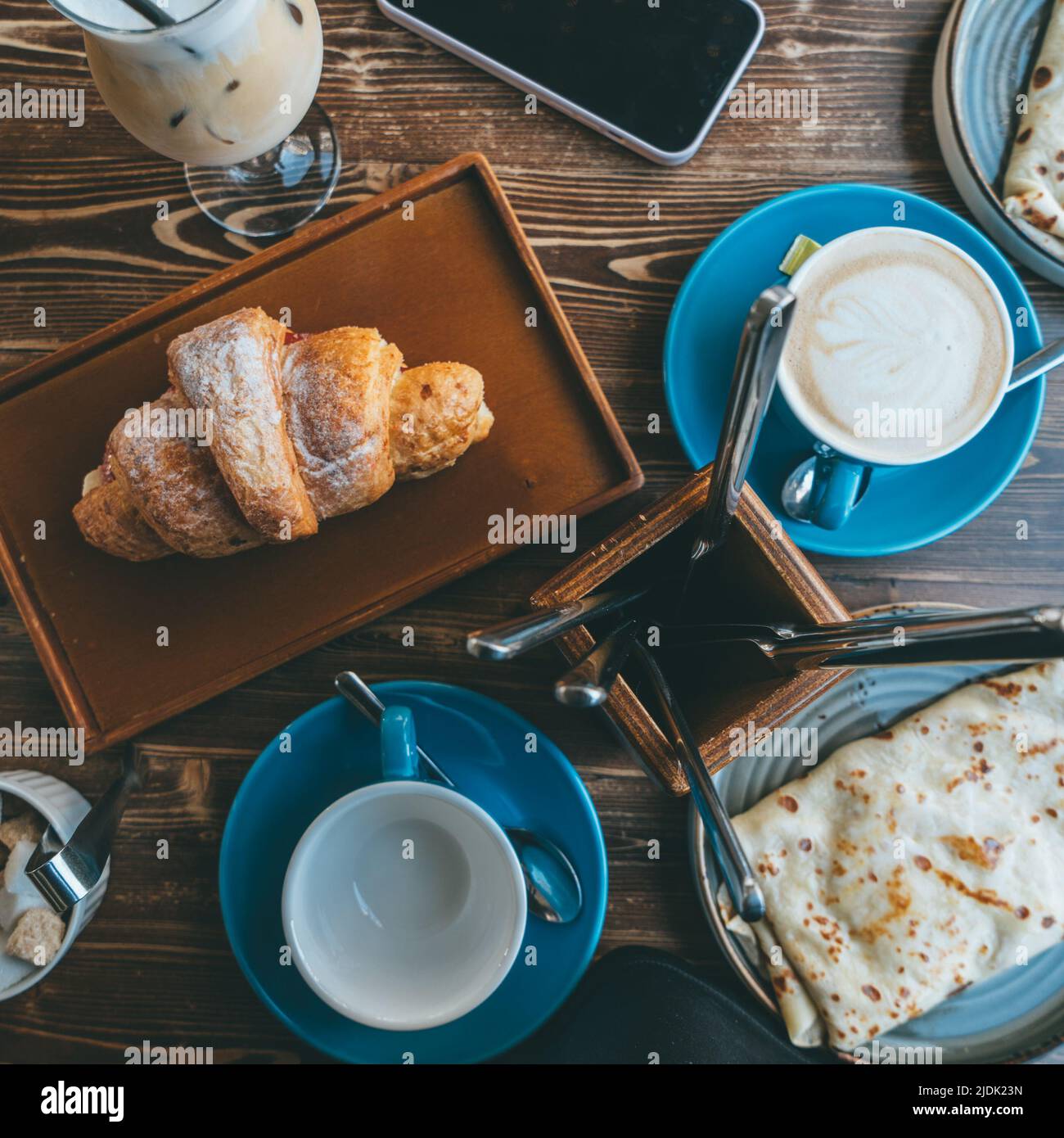 Vista dall'alto del tavolo in legno nel ristorante con appetitosa colazione di croissant, caffe' caldo e pancake. Foto Stock