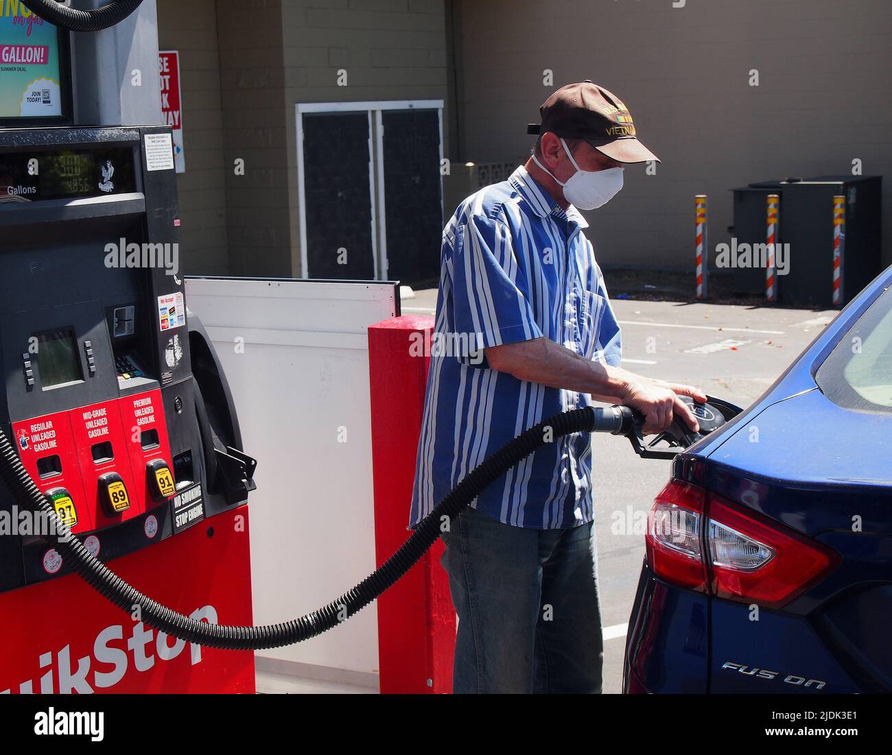 Senior indossa una maschera covid mentre pompa gas nella sua auto ibrida a un Quikstop a Castro Valley, California, giugno 2022 Foto Stock