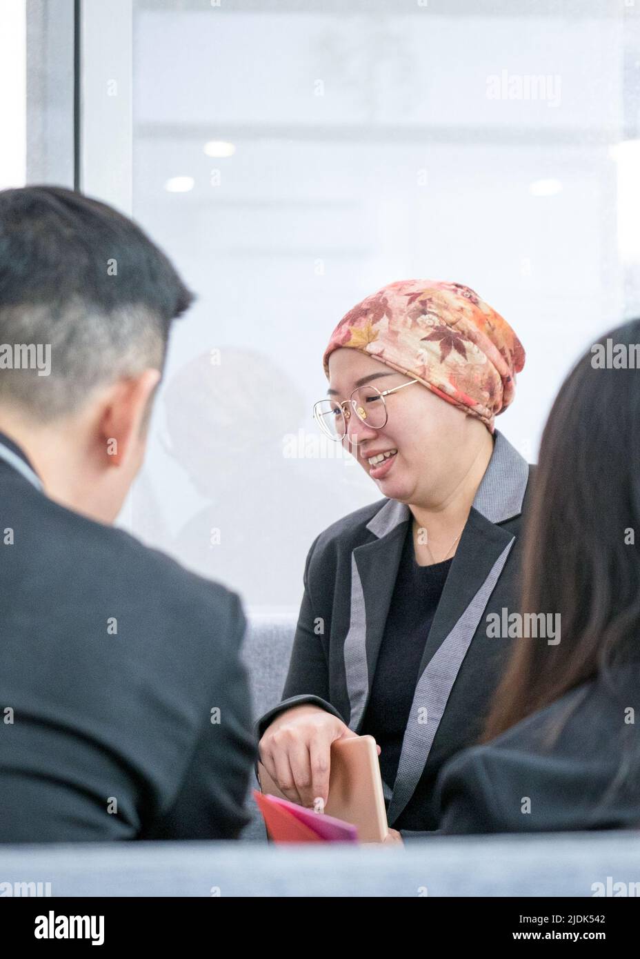 Donna d'affari asiatica sorridente mentre parla con i clienti. Ambiente d'ufficio moderno. Foto Stock