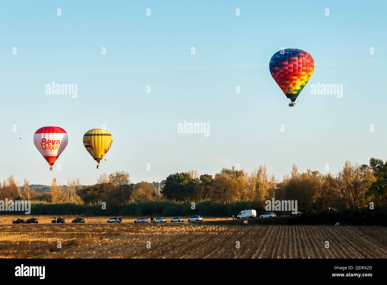 Coruche, Portogallo - 13 novembre 2021: Tre mongolfiere in volo nel tardo pomeriggio su campi agricoli e linea di alberi a Coruche, Portogallo Foto Stock