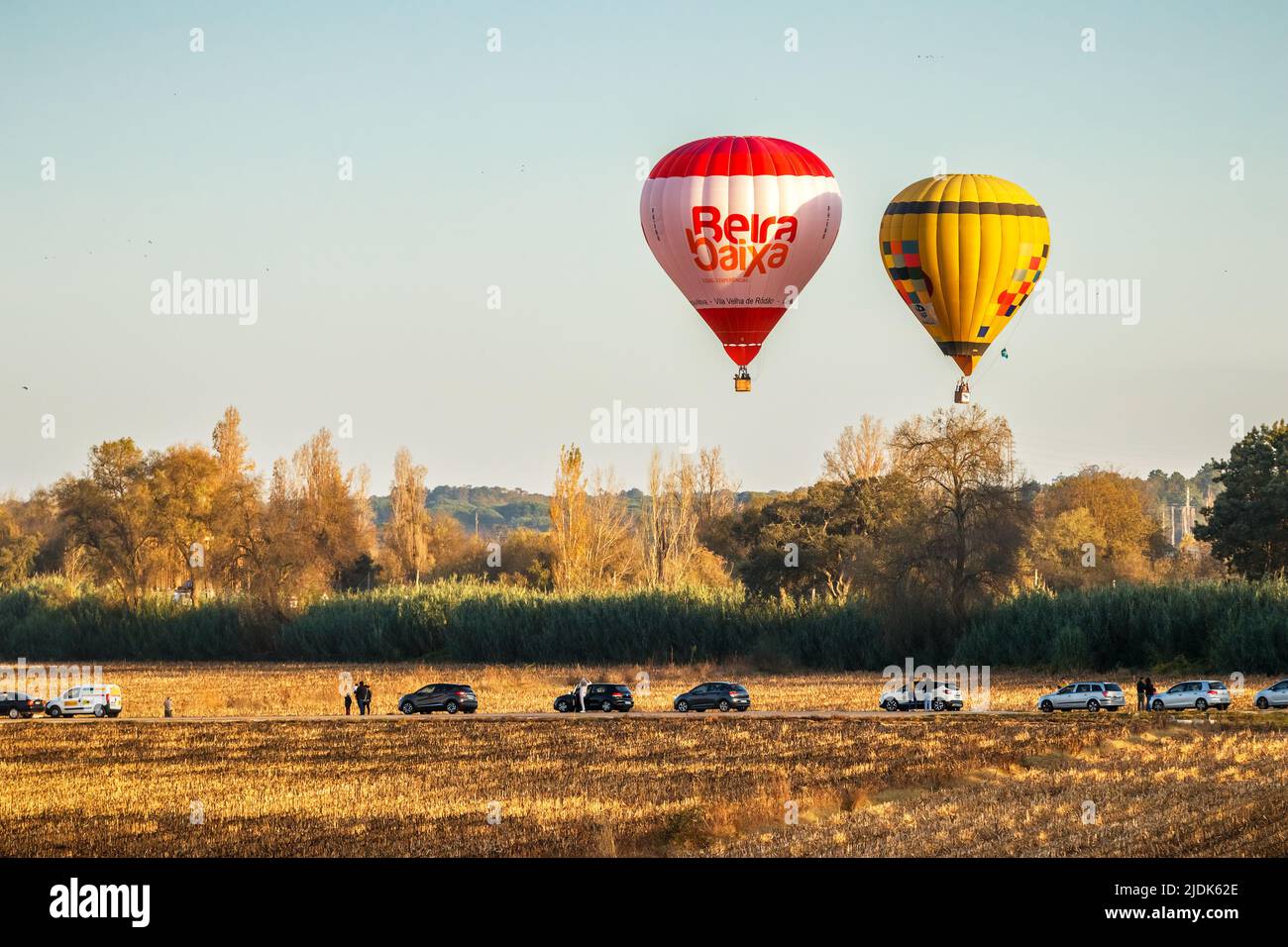 Coruche, Portogallo - 13 novembre 2021: Due mongolfiere che volano su alberi e terreni agricoli a Coruche, Portogallo, con auto parcheggiate e osservazione della gente Foto Stock