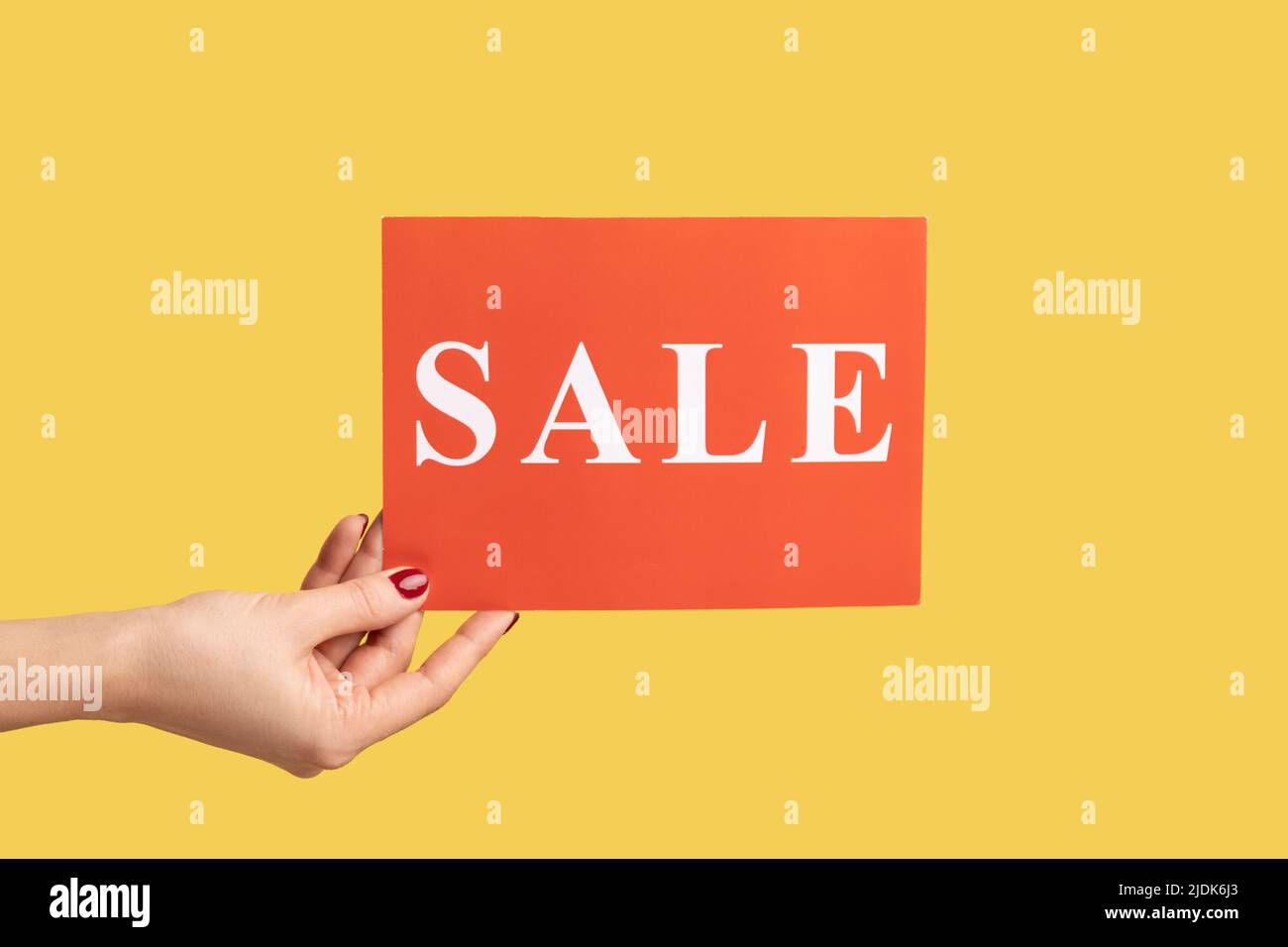 Profilo vista laterale primo piano della mano donna che tiene rosso vendita carta, mega shopping, Black friday sconti. Studio interno girato isolato su sfondo giallo. Foto Stock