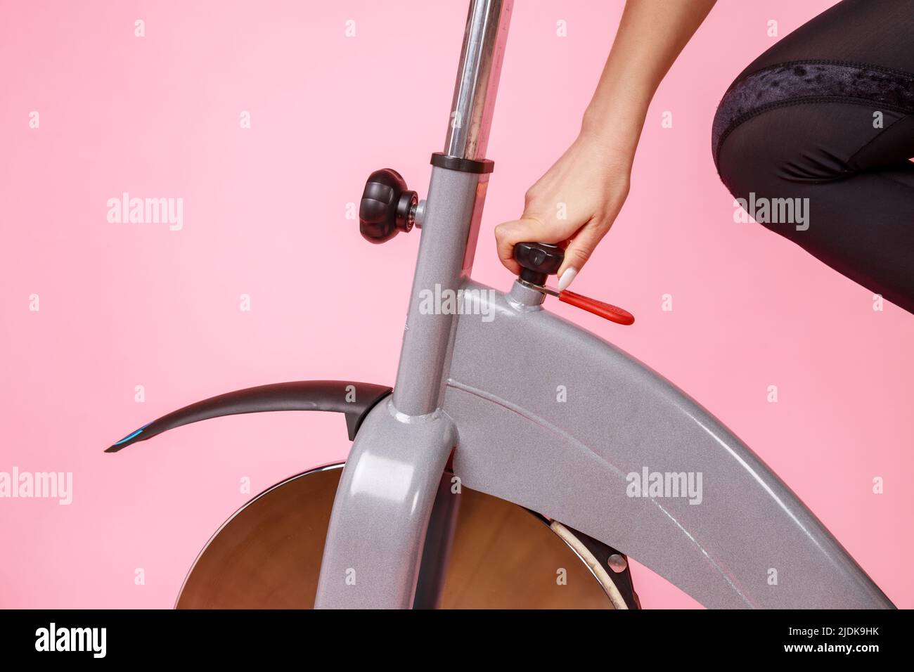 Ritratto closeup di donna mano che fissa la bici di esercitazione, facendo l'allenamento di sport, impostando una macchina di esercitazione. Studio interno girato isolato su sfondo rosa. Foto Stock