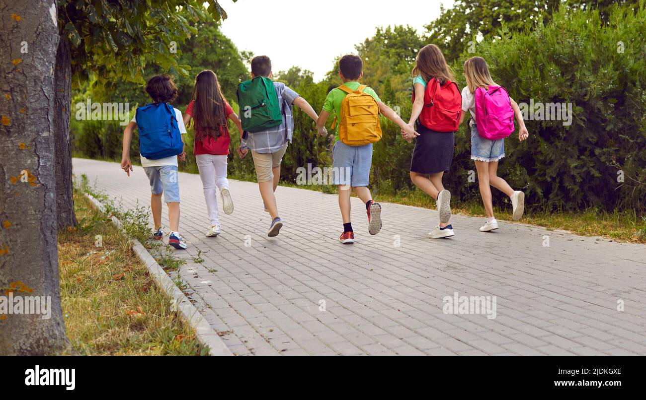 Vista posteriore di un gruppo di bambini felici con zaini colorati che corrono a scuola Foto Stock