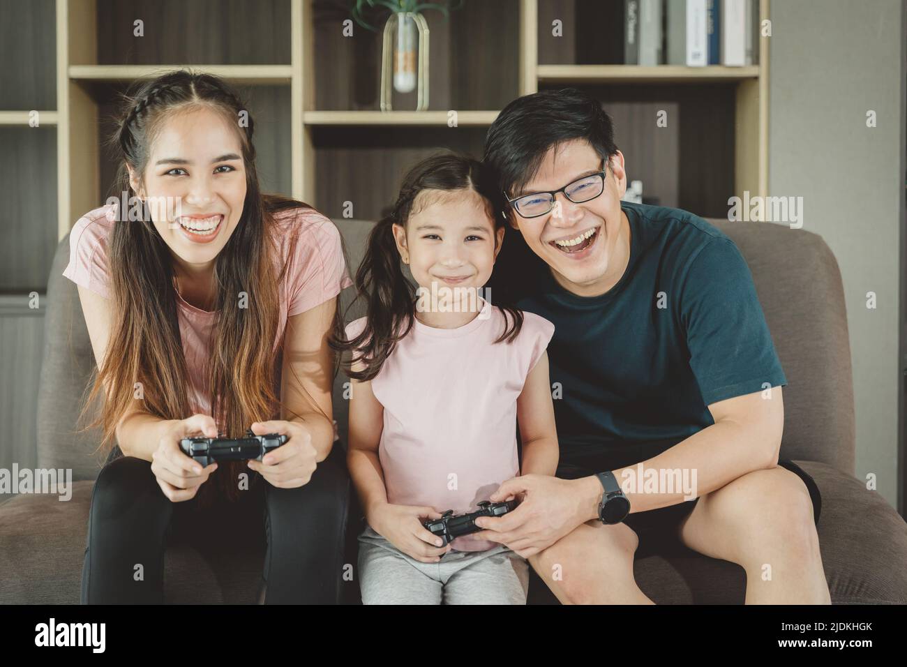 I genitori asiatici della famiglia con la figlia godono di giocare insieme che si diverte nel soggiorno del divano attività di vacanza a casa. Foto Stock