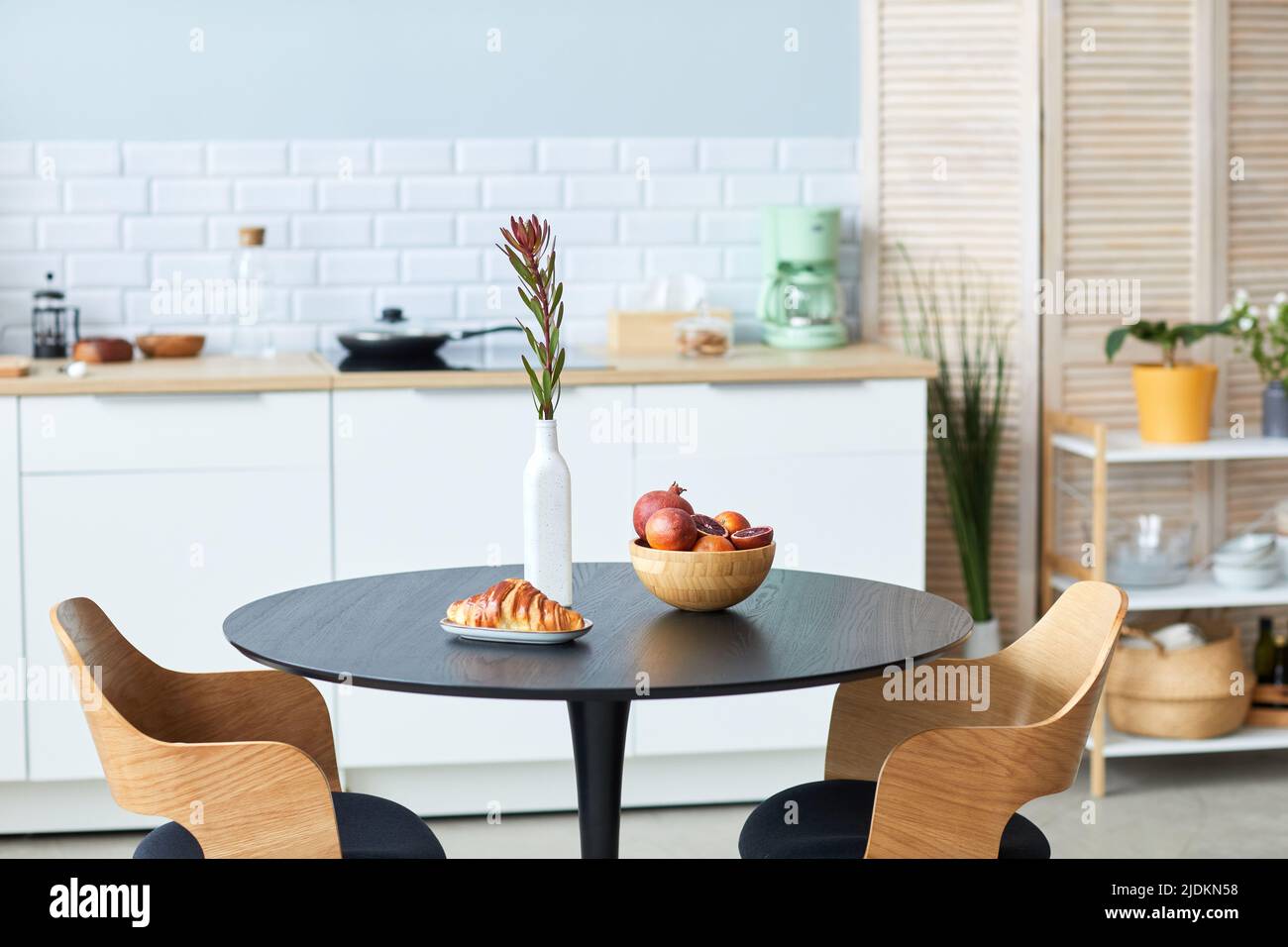 Primo piano di frutta e croissant su un elegante tavolo e sedie in legno con dettagli neri in interni minimal cucina, spazio copia Foto Stock