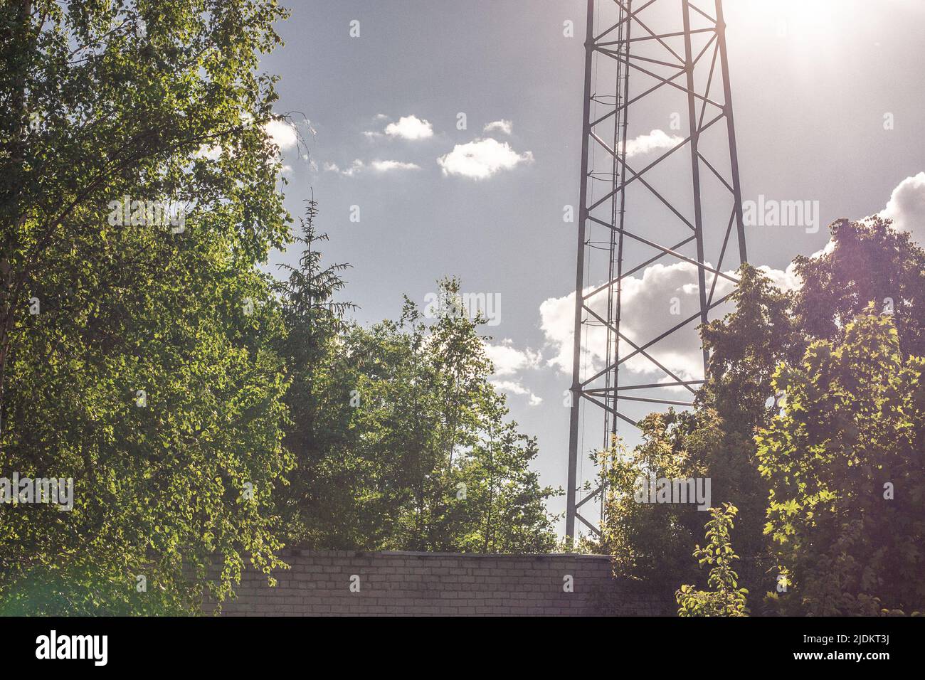 Calda giornata estiva con alberi verdi e un muro di mattoni accanto ad una torre TV in metallo con antenne. Foto Stock