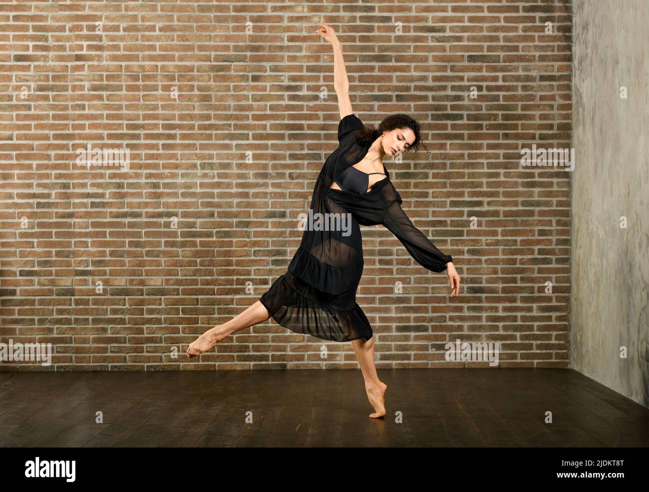 Corpo completo di ballerina femminile flessibile a piedi nudi in piedi su una gamba mentre si prova a ballare contro la parete di mattoni in studio Foto Stock