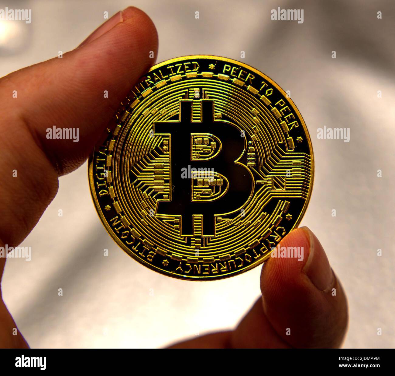 Due dita tengono una moneta metallica dorata di un Bitcoin su sfondo grigio Foto Stock