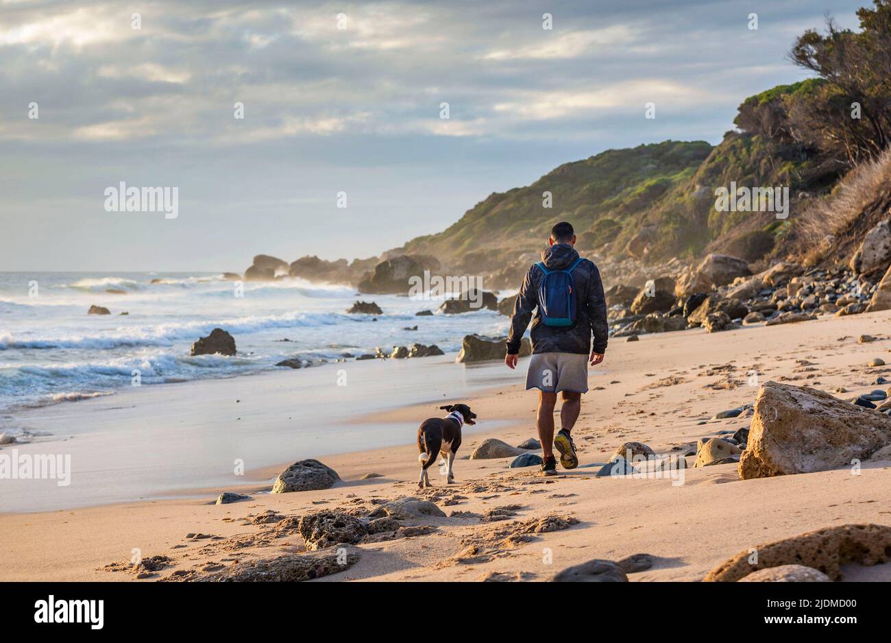 Il giovane sportivo e il suo cane camminano su una piccola spiaggia selvaggia vicino a Tarifa, Cadice, Andalusia, Spagna Foto Stock