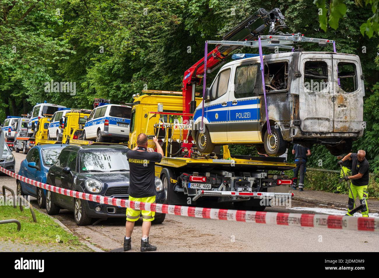 Monaco di Baviera, Germania. 22nd giugno 2022. Le auto della polizia bruciate che hanno preso il fuoco durante la notte sono prese da una società privata di traino. Gli autobus di squadra della polizia federale di sommossa sono parcheggiati davanti ad un hotel dove gli ufficiali di polizia sono alloggiati per la cima G7. Gli investigatori presumono che il fuoco sia stato causato da un'arsone. Credit: Peter Kneffel/dpa/Alamy Live News Foto Stock