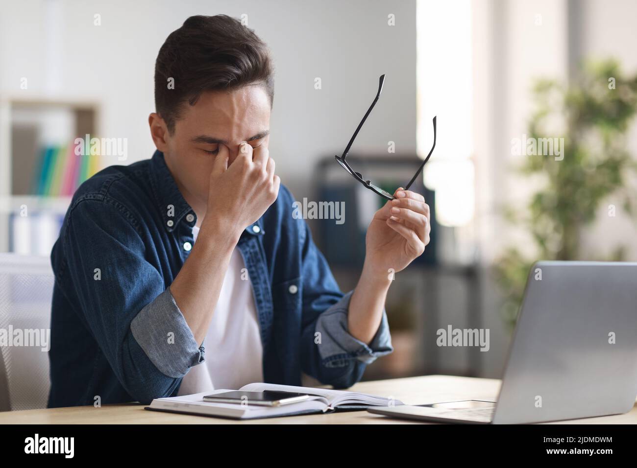 Gli occhi dei dipendenti dell'ufficio millennial si sfregano, stanchi dopo aver lavorato con il notebook alla scrivania Foto Stock
